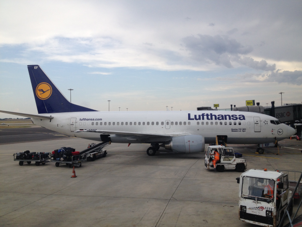 Lufthansa Airbus A320-200-Flugzeug am Frankfurt Airport mit Bodenbetriebsfahrzeugen, Verkehrskegeln und Informationsschildern unter einem bewölkten Himmel.
