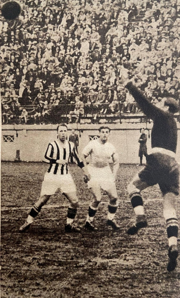Schwarzes und weißes Foto von Männern, die auf einem Feld Fußball spielen, mit Zuschauern auf den Tribünen und einer Wand im Hintergrund, beschriftet mit 'Newcastle United v West Bromwich Albion'.