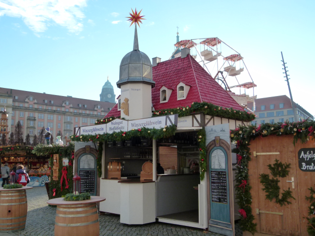 Ein kleines Gebäude mit rotem Dach und einem Riesenrad davor, umgeben von Festschmuck und Menschen auf einem Oktoberfest in München, Deutschland.