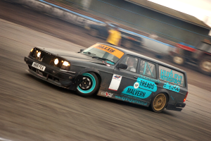 Ein Auto fährt eine Rennstrecke entlang mit einem Fahrer darin, umgeben von anderen Fahrzeugen, mit einem unscharfen Hintergrund, der hohe Geschwindigkeit andeutet.