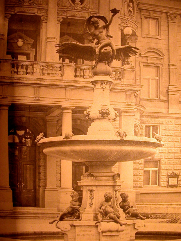 Altes Schwarz-Weiß-Foto eines Brunnens mit Skulpturen vor einem mehrstöckigen Gebäude mit Fenstern, Säulen, Geländern, Lichtern und einer Tür, mit einem Wasserzeichen über das Bild.