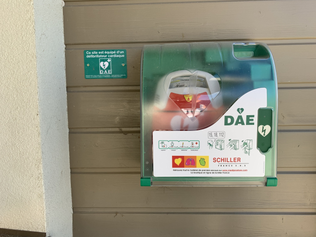Ein grüner und weißer Kasten an einem Gebäude mit einem 'AED'-Aufkleber, der auf einen automatischen externen Defibrillator hinweist.