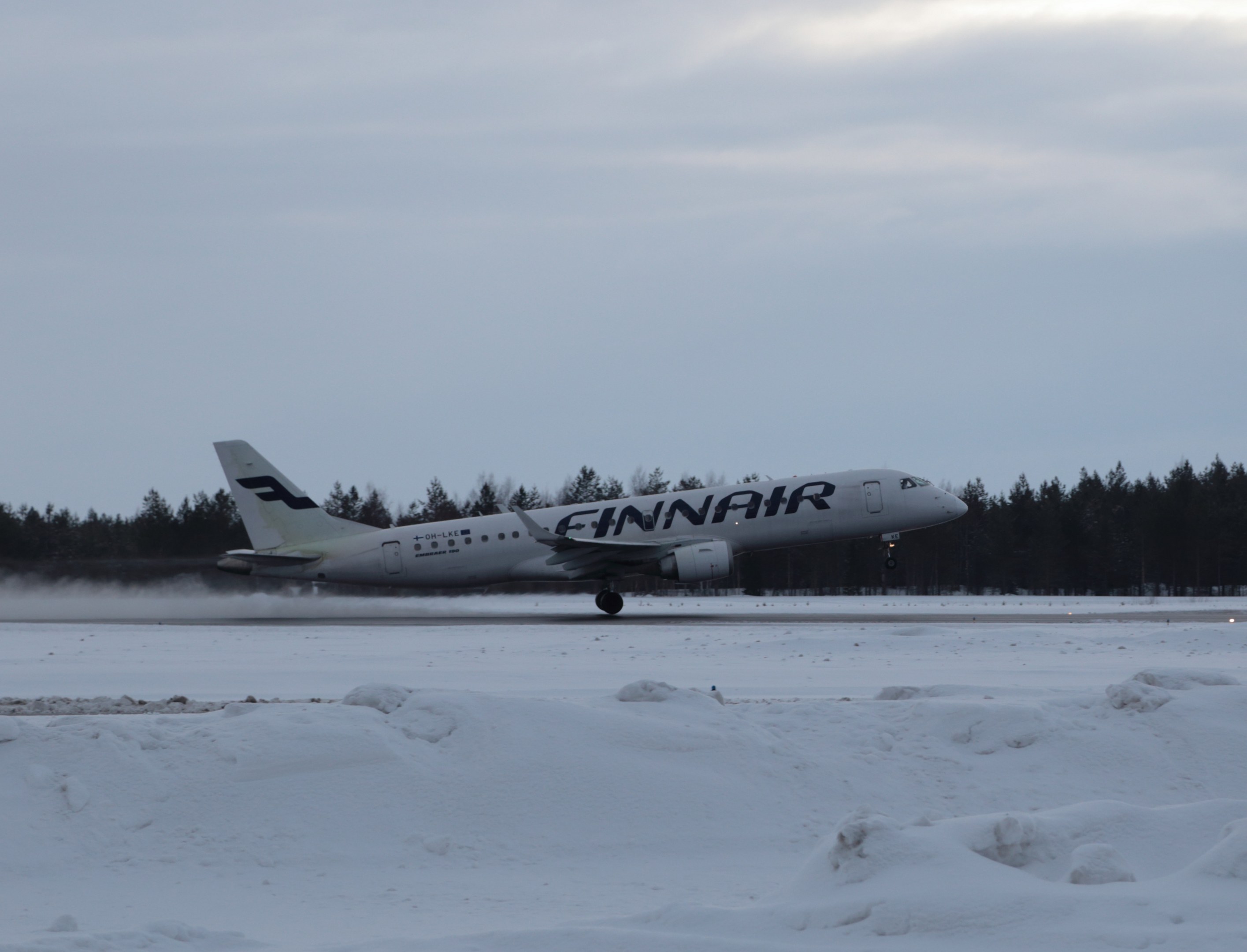 Finnair Airbus A320-200 auf einer verschneiten Landebahn am Helsinki Airport mit Bäumen und einem klaren blauen Himmel im Hintergrund.