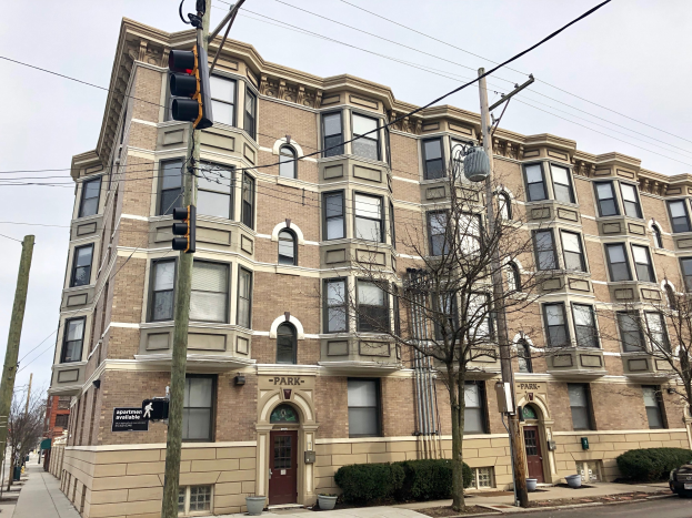 Große Mietwohnung mit der Bezeichnung "Park Apartments for Rent in Chicago, IL" an einer Straßenkreuzung mit Bäumen, Topfpflanzen, Strommasten, einer Ampel, einem Auto und einem bewölktem Himmel.