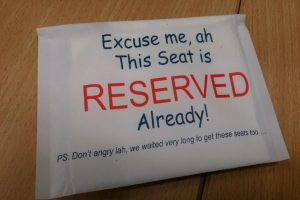 Ein hölzerner Tisch mit einem handgeschriebenen Zettel auf Papier, auf dem steht: "Entschuldigung, dieser Sitz ist bereits reserviert."