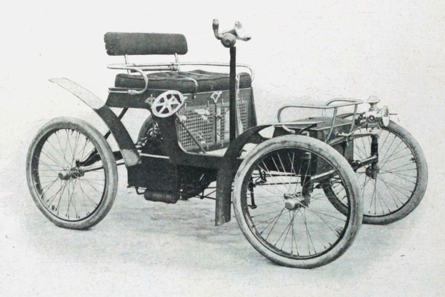 Vintage-Foto in Schwarz-Weiß von einem frühen Elektroauto aus den 1900er-Jahren mit schlankem, aerodynamischem Design, großem runden Scheinwerfer, geschwungener Dachlinie, vier großen Rädern, prominentem Heckmotor, leichtem Sitzbezug und einem Armaturenbrett mit Knöpfen und Drehreglern.