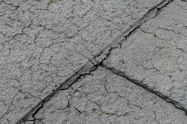 Nahaufnahme einer gebrochenen und verwitterten Straßenoberfläche mit tiefen, breiten Rissen.