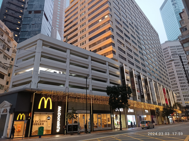 Ein McDonald's-Restaurant auf einer belebten Stadtstraße mit hohen Gebäuden, Fahrzeugen, Fußgängern, Bäumen und einem klaren Himmel.