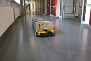 Ein Roboter, der zum Bodenreinigen entworfen wurde, steht auf dem Boden eines Gebäudes, umgeben von Wänden, Türen, Lampen und anderen Gegenständen.