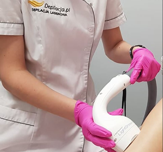 Eine Frau in einem weißen Hemd und pinken Handschuhen bedient ein weißes Laser-Haarrentferungsgerät auf ihrer Haut, vor einer Wand stehend.