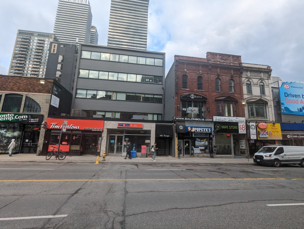 Stadtstraße mit hohen Gebäuden, fahrenden Fahrzeugen, Fußgängern, einem Fahrrad, einem Feuerhydranten und Schildern mit der Aufschrift "Mietwohnungen zu vermieten" an der 5901 S Elmwood Avenue, Toronto.