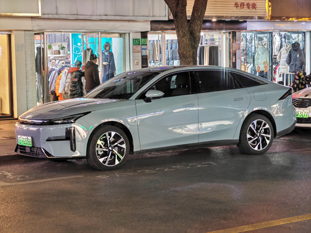 Ein Mitsubishi Lancer EV auf einer Straße bei Nacht, umgeben von Gebäuden, Geschäften, Schaufensterpuppen, Schildern und Lichtern.
