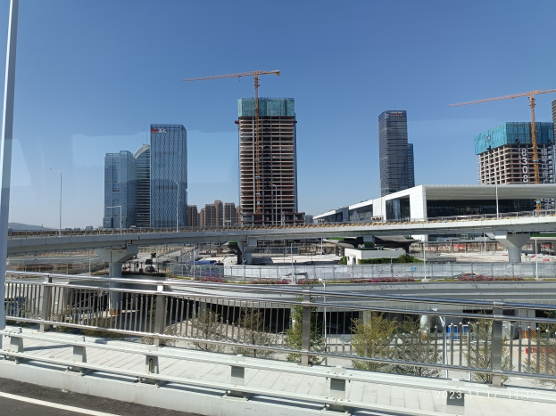 Eine Stadtpanorama-Ansicht von einer Brücke aus, mit Gebäuden, Baukränen, Straßeninfrastruktur, Fahrzeugen und einem klaren Himmel.