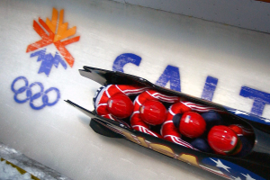 Ein Rodler in einem Fahrzeug bei den Olympischen Spielen, mit einer dekorierten Wand mit Text und einem Gemälde im Hintergrund.