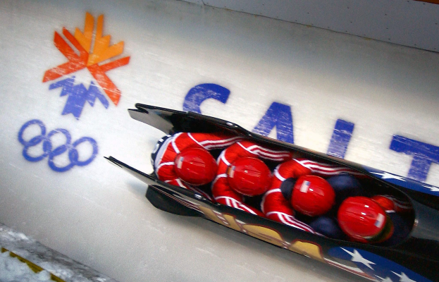 Ein Rodler in einem Fahrzeug bei den Olympischen Spielen, mit einer dekorierten Wand mit Text und einem Gemälde im Hintergrund.