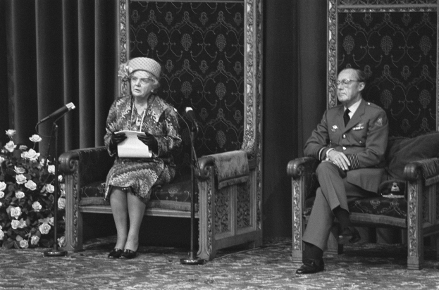 Schwarzes und weißes Foto von Queen Elizabeth II und Prinz Philip, die auf Stühlen einander gegenüber sitzen, mit Mikrofonen vor ihnen, die Queen h├Ąlt ein Blatt Papier, ein Blumenbouquet links und Vorh├Ąnge im Hintergrund.