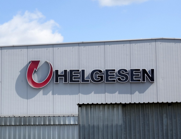 Helgesen sign on a building exterior with text reading "Helgesen investiert 1,5 Milliarden USD in den USA" against a cloudy sky.