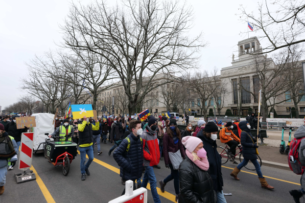 Eine große Gruppe von Menschen marschiert auf einer Stadtstraße in Washington, D.C., mit Schildern und Fahrrädern unter einem klaren blauen Himmel.