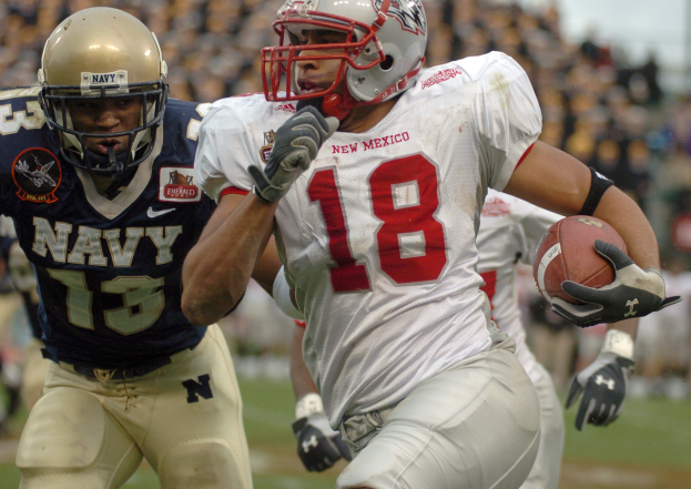Ein Fußball-Spieler in einem Helm und Handschuhen rennt mit dem Ball während eines Spiels, mit einem unscharfen Hintergrund, der eine schnelle Bewegung andeutet.
