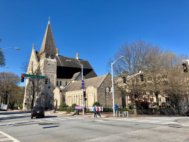 Große Kirche mit Turm an einer Straßenkreuzung, beschriftet als St. Lukes Episcopal Church, umgeben von Gebäuden und städtischen Elementen unter einem klaren blauen Himmel.