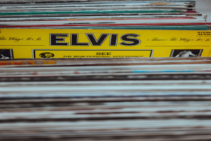 Ein ordentlich gestapelter Haufen Elvis-Presley-Platten auf einem Tisch, mit sichtbaren Titeln und einem leicht unscharfen, träumerischen Hintergrund.