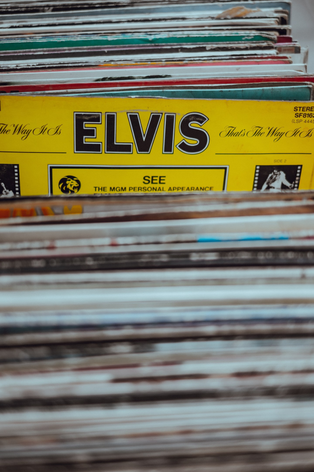 Ein ordentlich gestapelter Haufen Elvis-Presley-Platten auf einem Tisch, mit sichtbaren Titeln und einem leicht unscharfen, träumerischen Hintergrund.