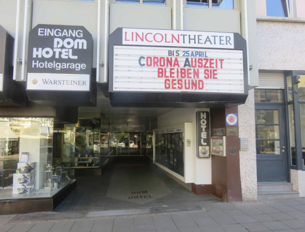 Außenansicht des Lincoln Theaters in Berlin, Deutschland, mit Glasfenstern und -türen sowie einer Texttafel und einem belebten Inneren durch den Eingang sichtbar.