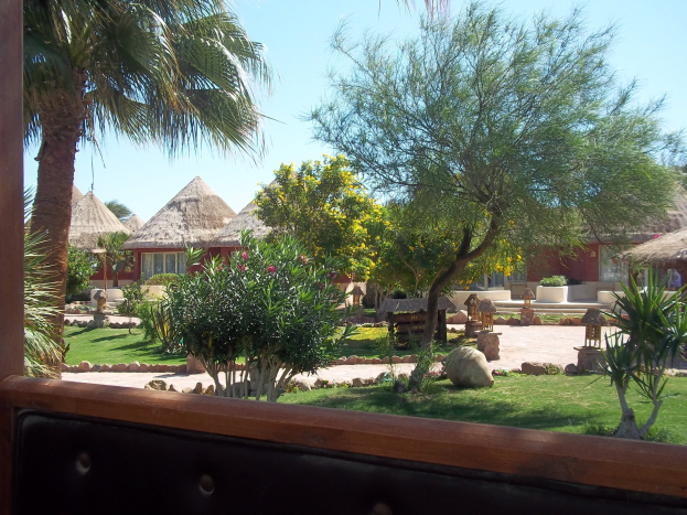 Ein Resort-Szenario mit Hütten, Grünzeug, Felsen, einer Bank und Himmel.