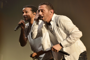 Zwei Männer in legerer Kleidung auf der Bühne, jeder hält ein Mikrofon.