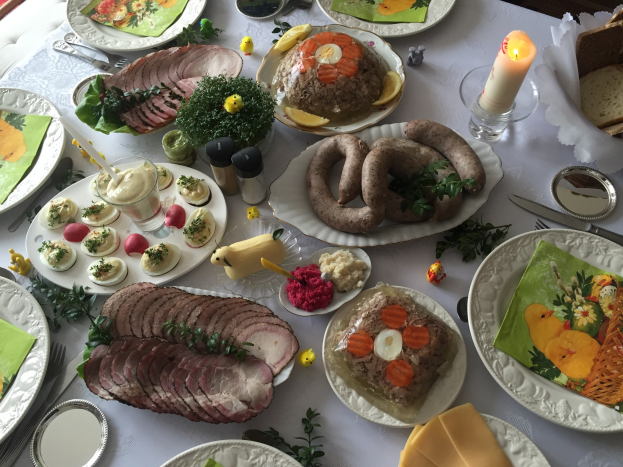 Ein langer Tisch mit verschiedenen Gerichten, Besteck und Kerzen, umgeben von Stühlen, das für ein traditionelles deutsches Osteressen steht.