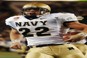 Ein Fussballspieler in Uniform und Helm läuft mit dem Ball in der Hand, Hintergrund unscharf, um Geschwindigkeit anzudeuten.