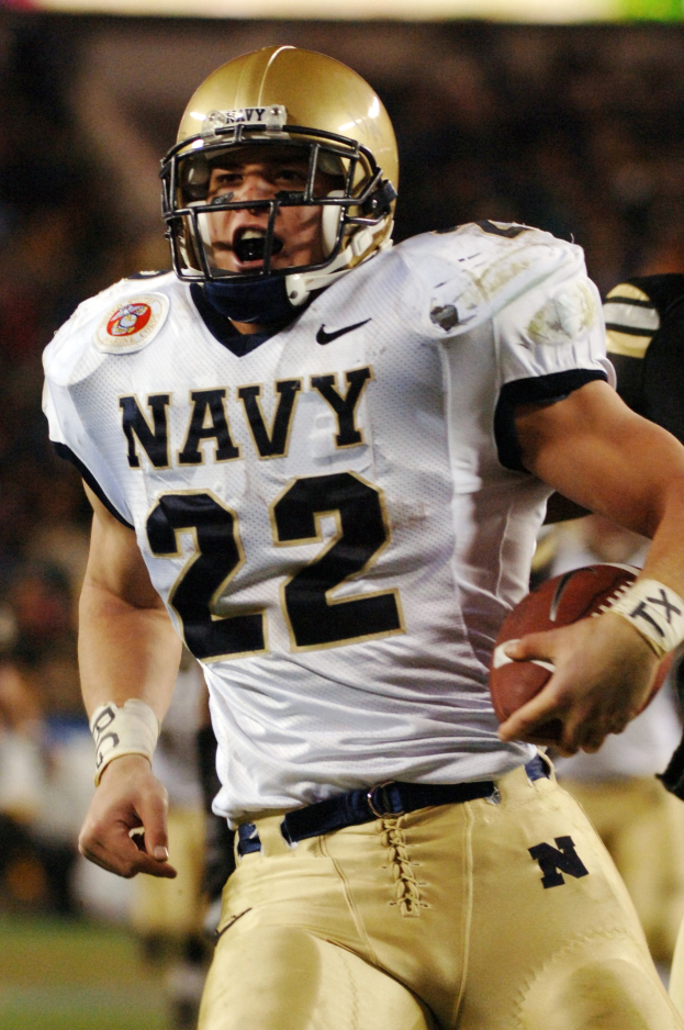 Ein Fussballspieler in Uniform und Helm läuft mit dem Ball in der Hand, Hintergrund unscharf, um Geschwindigkeit anzudeuten.