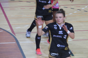 Eine Gruppe von Frauen in Sportkleidung und -schuhen spielt Volleyball auf einem Platz.