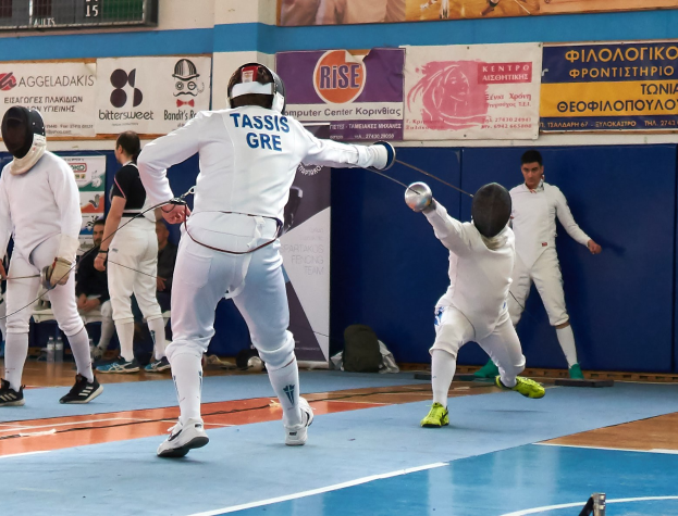 Gruppe von Fechtern in einer Turnhalle mit Wandbannern, Zuschauern und einem Scoreboard oben.