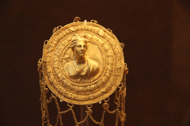 Goldene Medaille mit einer Frauengestalt auf dunklem Hintergrund, mit feiner Verzierung und luxuriösem Aussehen.