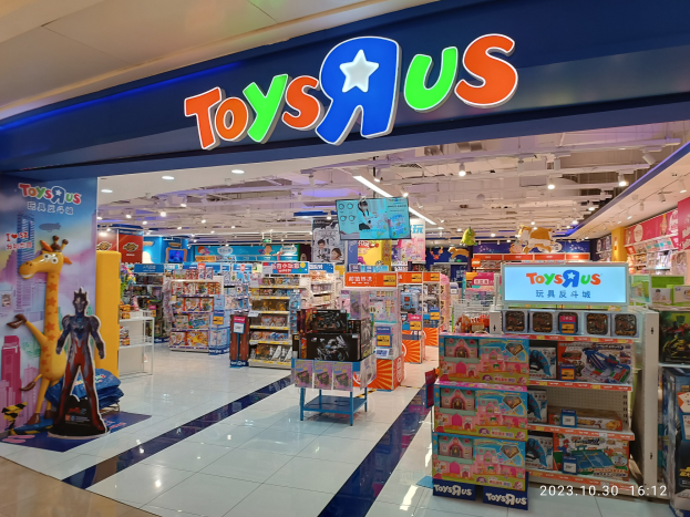 Ein Toys R Us Geschäft in einem Einkaufszentrum mit Regalen voller Spielzeug, Deckenbeleuchtung, einem sichtbaren Ladenschild und einem Wasserzeichen in der rechten unteren Ecke.