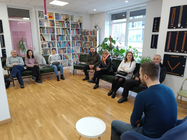 Eine Gruppe von Menschen sitzt um einen Tisch in einem Raum mit Bücherregalen, Pflanzen und einem Fenster, die während einer Workshop-Veranstaltung über die Zukunft von Gesundheit und Wohlbefinden in Berlin, Deutschland, diskutieren.