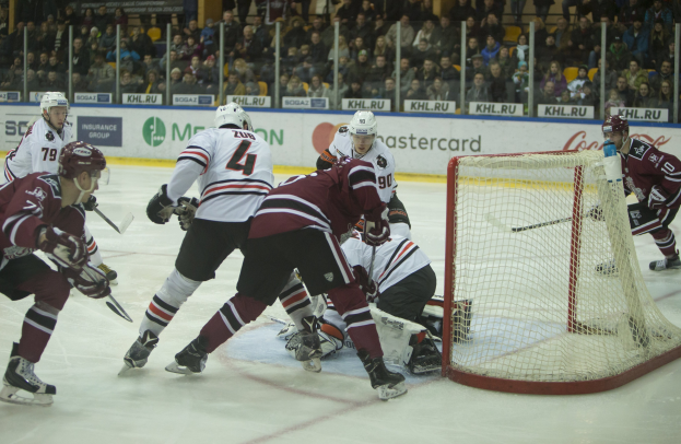 Eine Gruppe von Menschen, die Hockey auf einem Eisplatz spielen, tragen Sportkleidung und halten Stöcke, mit einem Torpfosten auf der rechten Seite und Zuschauern im Hintergrund.