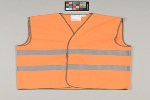 Leuchtend orangefarbene Sicherheitsweste mit reflektierenden Streifen und einem Anhänger auf einem grauen Hintergrund.