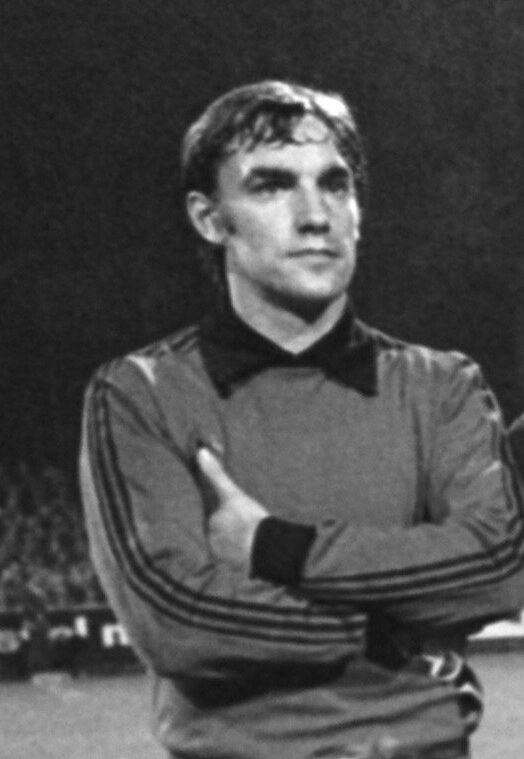 Schwarzes und weißes Foto eines Mannes, der mit verschränkten Armen auf einem Fußballfeld steht und von sitzenden Zuschauern umgeben ist, der als legendärer Torwart von Manchester United gilt, der im Alter von 89 Jahren verstorben ist.