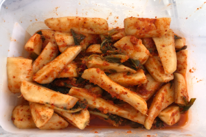 Ein Kunststoffbehälter voller goldbraun frittierter Tofu und bunter Gemüse, darunter grün, gelb und rot, auf einem Tisch.