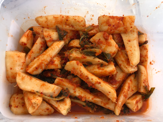 Ein Kunststoffbehälter voller goldbraun frittierter Tofu und bunter Gemüse, darunter grün, gelb und rot, auf einem Tisch.