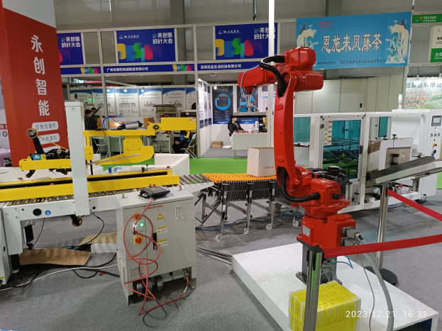 Gruppe von Robotern auf einem Tisch in einer Fabrikeinrichtung umgeben von Maschinen, Kabeln, Platinen und beleuchteten Bauteilen, mit Menschen im Hintergrund.