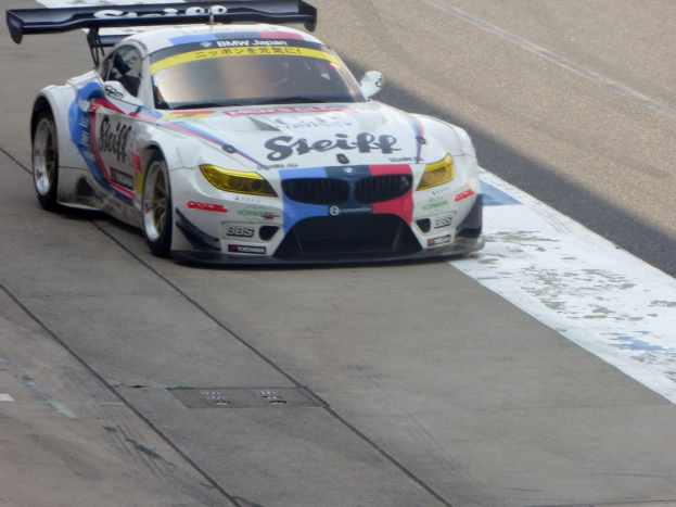 Ein strahlend blauer und weißer BMW Z4 GT3 Rennauto mit großen glänzenden Rädern auf einer Rennstrecke, mit einer schlanken, aerodynamischen Gestaltung und prominenten BMW-Logos.