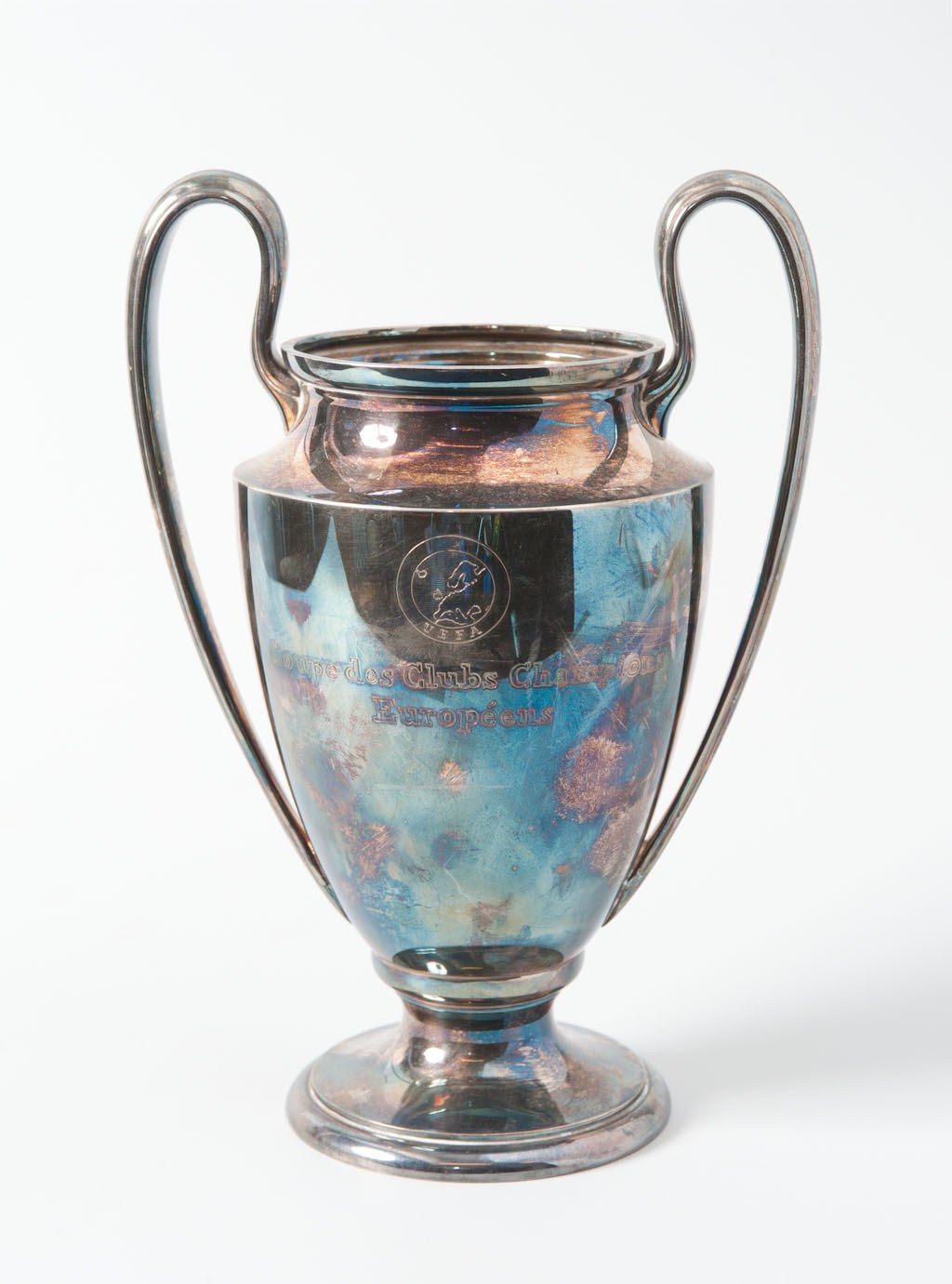 Der UEFA-Champions-League-Pokal, ein silberner und blauer Stahlbecher mit zwei Griffen, der mit "UEFA Champions League" beschriftet ist, vor einem weißen Hintergrund dargestellt.