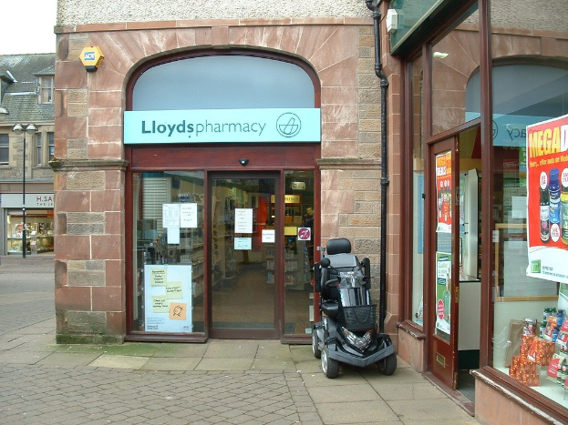 Ein Apothekenladen mit einem Fahrzeug davor und einem Gebäude links daneben.