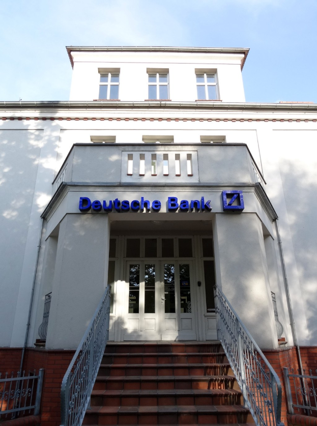 Das Deutsche Bank Gebäude in Frankfurt, Deutschland, mit sichtbaren Fenstern, Türen, Treppen, Geländern und einem Namensschild gegen einen klaren blauen Himmel.
