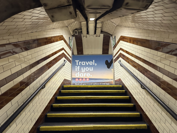 Eine Treppe in einer U-Bahn-Station mit Geländern auf beiden Seiten, die zu einem Schild führt, auf dem "Reise, wenn du wagst" steht.
