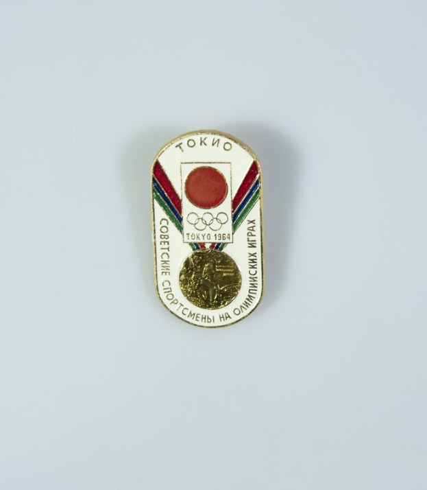 Ein Abzeichen mit der Aufschrift "Tokyo 1964 Olympische Spiele" und eine goldene Medaille mit rot-weiß-blauen Streifen auf weißem Hintergrund.