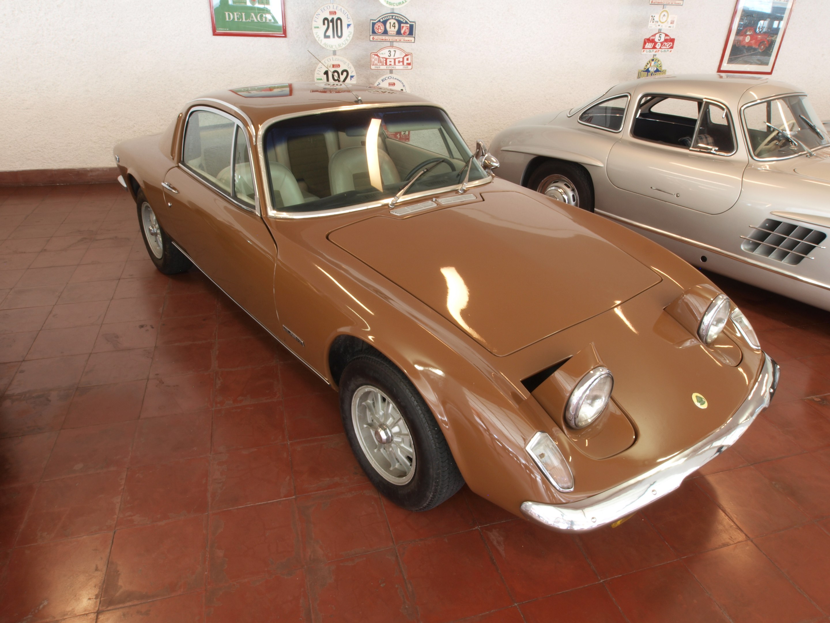 Zwei klassische Autos, ein Ferrari 250 GT und ein Ferrari Dino 246 GT, Seite an Seite in einem Raum mit Rahmenfotos und Tafeln an der Wand dahinter geparkt.